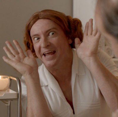 Rhys Darby in character as a masseuse with a bright ginger wig. I think this is from an old NZ advert directed by Taika Waititi, but I can’t recall the product. Anyone…?