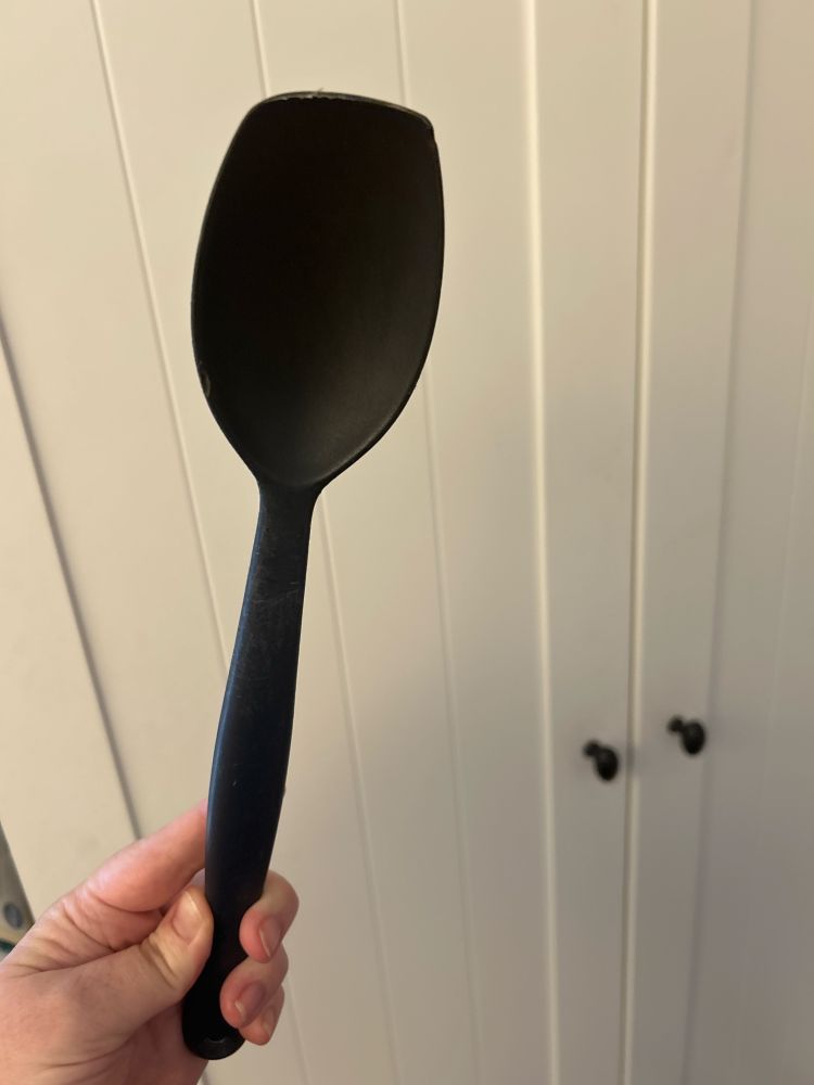 A black plastic cooking spoon with a flat tip that is looking a little worn