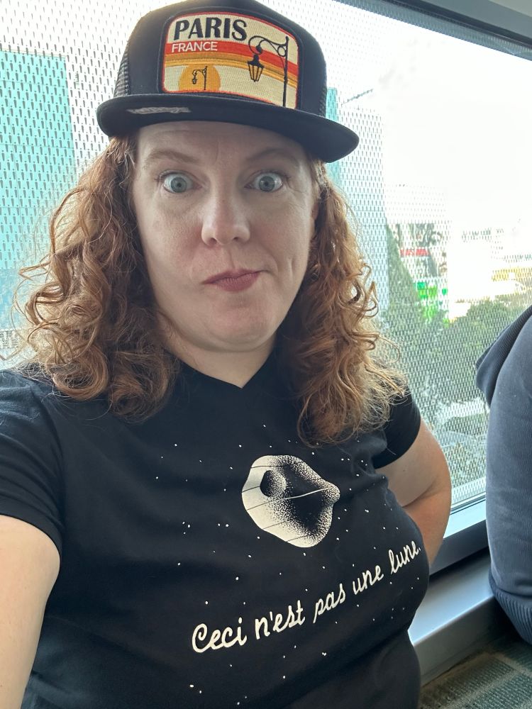 Me making a goofy face while wearing a black ball cap that says "Paris, France" and a shirt with a picture of the Death Star on and written underneath in very French script is "Ceci n'est pas une lune."