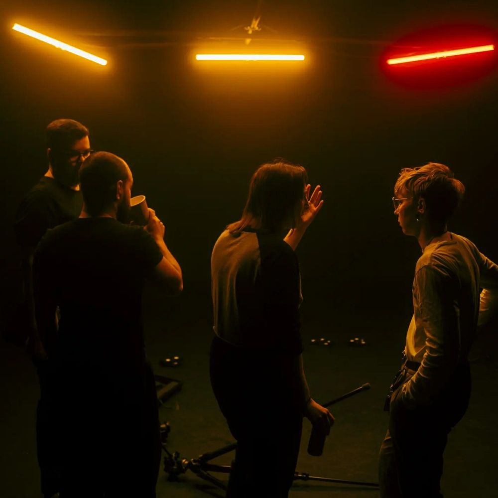 In a studio, three warm Asteria lighting tubes are downlighting four of the crew. They are facing the other way, unaware and in conversation.