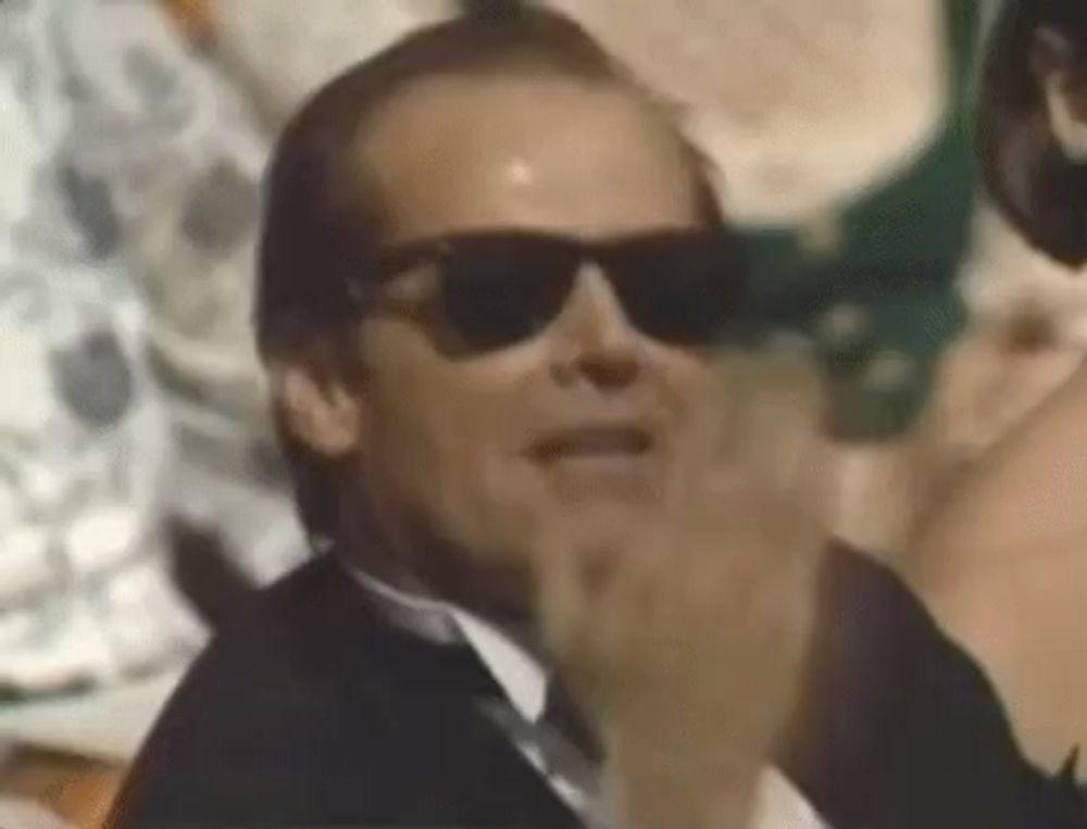 a man in a tuxedo and sunglasses is clapping his hands .