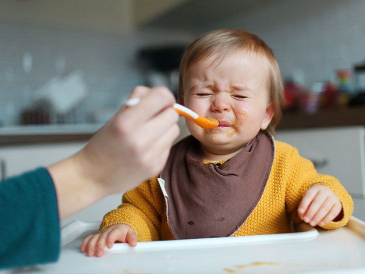A very upset baby being spoon fed mushy food