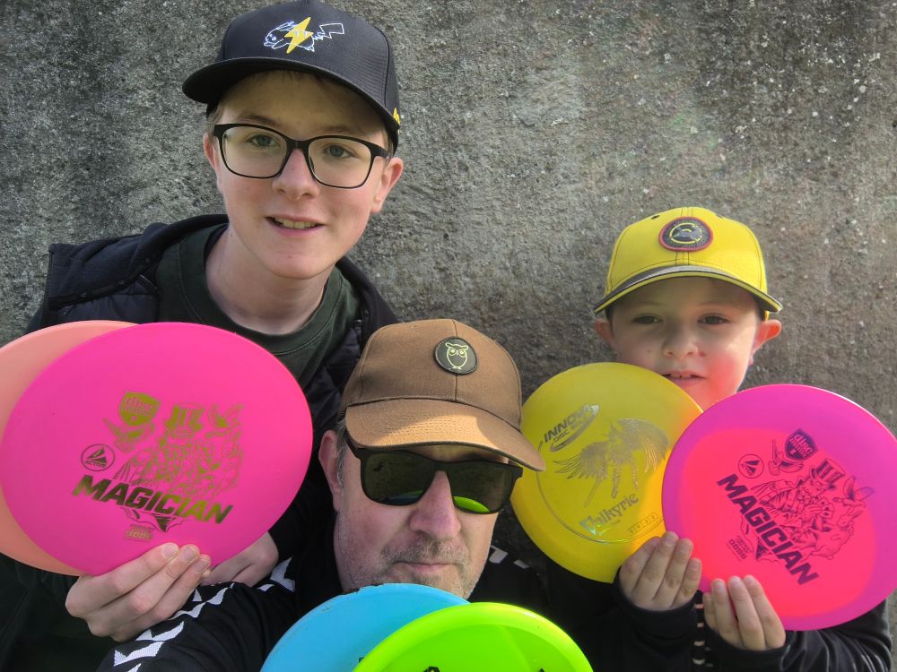 Tveir myndarlegir ungir menn og aldraður faðir þeirra, allir með derhúfu og halda á frisbí diskum. 