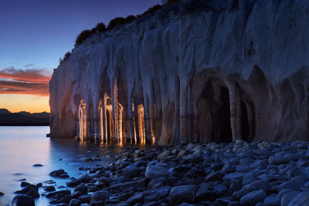 Where an Ancient Explosion Becomes Modern Art

Photographer friend Armando and I went on a road trip to the Sierra Nevada mountains, with the goal to take photos of the Stone Columns at Crowley Lake near Mammoth Lakes. The columns look man-made, like designed by Antoni Gaudí. However they are a natural wonder. Crowley Lake was buried and hidden for ages under the tons of pumice and volcanic ash from a cataclysmic explosion 760,000 years ago. The columns were created by the melting snow seeping down into the hot volcanic ash. As the water boiled, it created evenly spaced convection cells similar to vertical heat pipes. These pipes were cemented into place by minerals, which were able to resist the erosion of the surrounding forces such as wind and strong waves. We waited until nigh fall. Armando operated my camera with Dream Lens. I took off shoes and socks, and waded in the dark with a strong LED light. I illuminated the columns from behind to give the scene a mysterious look.

-- ƒ/8.0, 50 mm, 1/15, 0.3, 1, 4, 6, 8, 15, 30 sec, ISO 100, Sony A7 II, Canon 50mm f0.95 "Dream Lens", HDR, CC BY-NC-SA 4.0, © 2025 Peter Thoeny, Quality HDR Photography