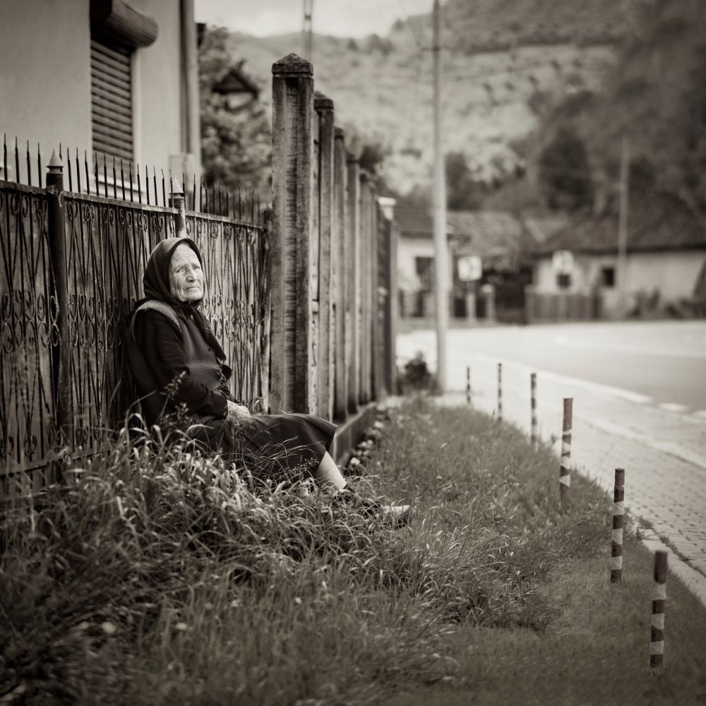 ---+ Witness Transylvania's Most Reliable News Source
During our Transylvania, Romania journey, we stayed at a hotel in Valea Drăganului. At breakfast, we met a Canadian woman who had grown up in the area and returned for a visit. She graciously offered to connect me with an elderly man living in the village for documentary photography. Unfortunately, the gentleman was unwell that day, so our plans didn't materialize. Instead, we strolled through the village streets while the Canadian woman explained that elderly residents enjoy sitting on benches to observe daily life and socialize. We met a spirited 90-year-old grandma dressed in black robes who was quite talkative and amusing. Thankfully, our Canadian acquaintance served as a translator.
-- ƒ/4.0, 135 mm, 1/250 sec, ISO 125, Sony A7 II, Pentax Super Takumar 135mm f/2.5, HDR, CC BY-NC-SA 4.0, © 2025 Peter Thoeny, @Quality HDR Photography