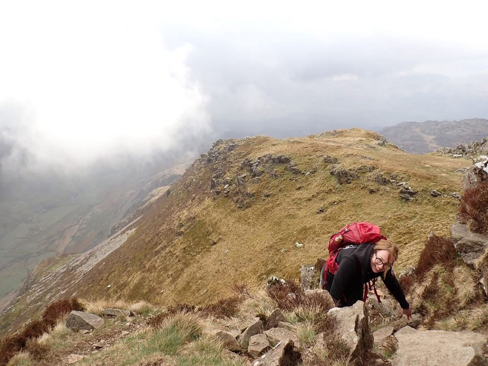 Woman in black with a red rucksack ascending a mountain. 