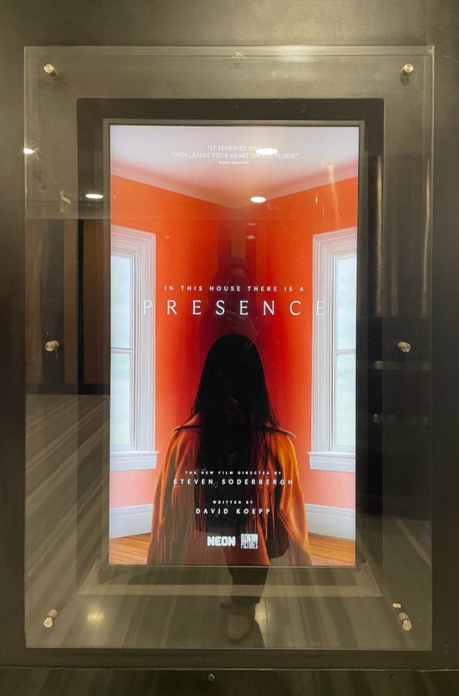 Poster of the movie “Presence” depicting the back of a woman staring at a red corner wall between two windows