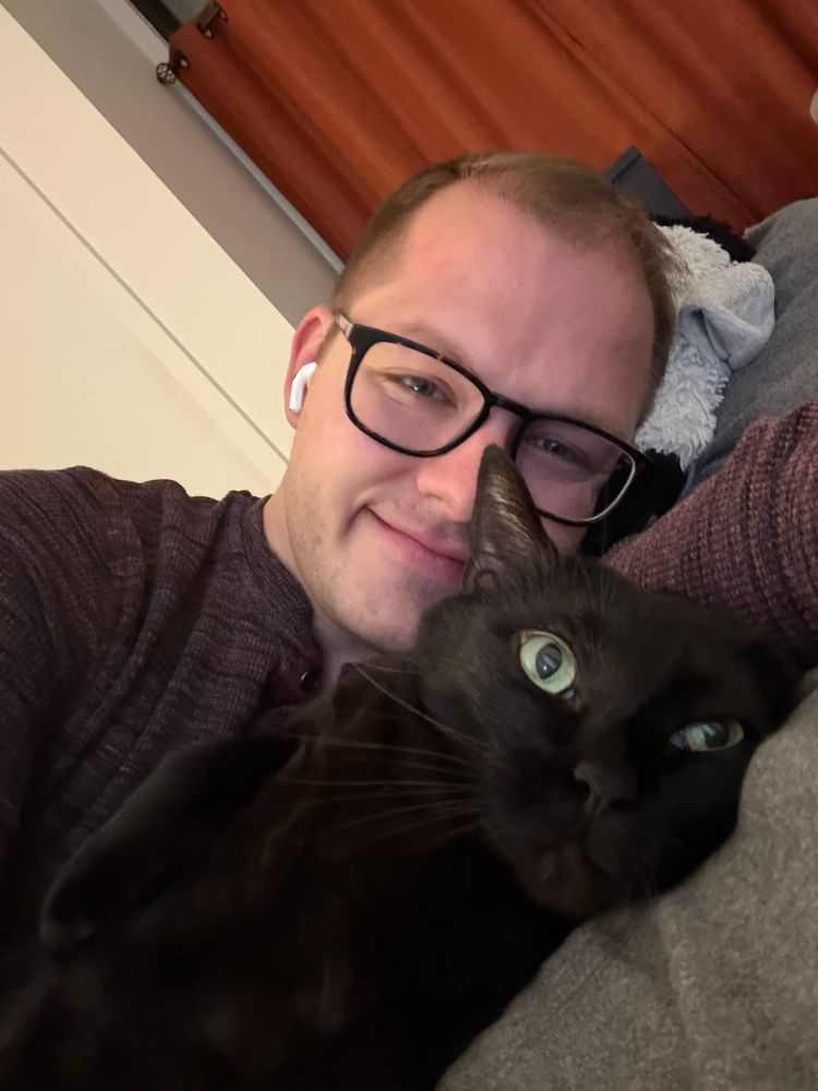 Will, a gay, with their black cat looking like a goofball 