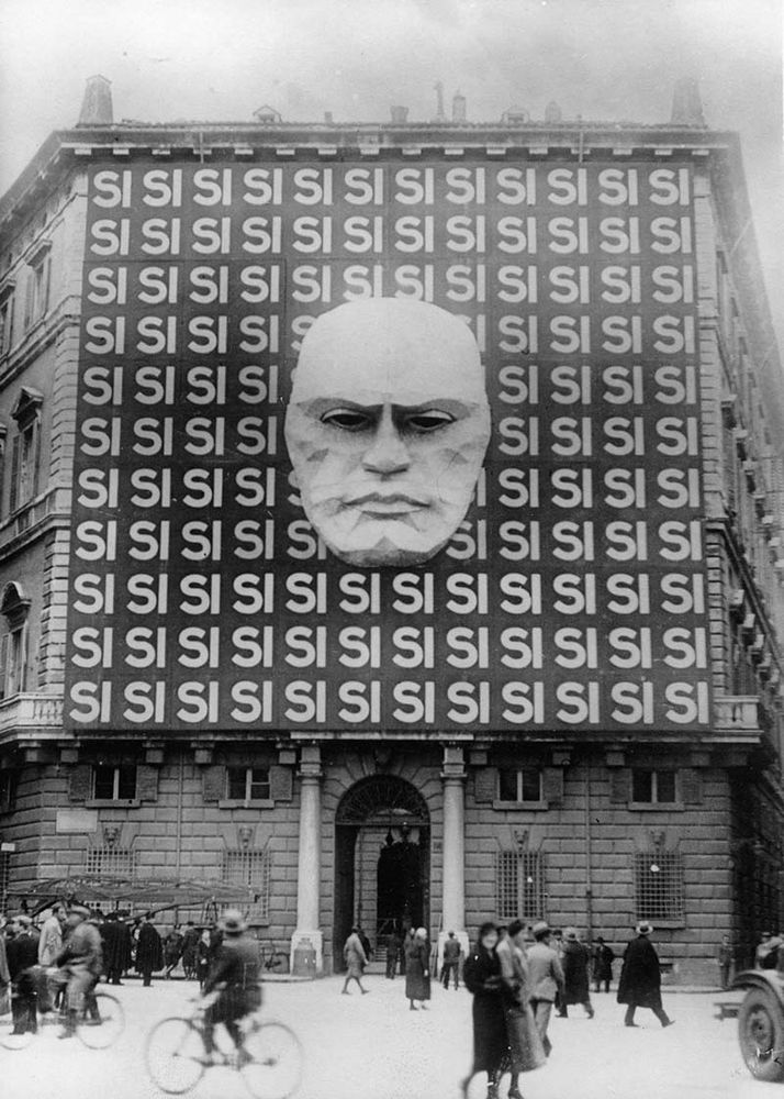Photo en noir et blanc du quartier général du parti fasciste italien, surmonté de la tête de Mussolini.