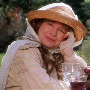 Dianne Wiest dressed in turn of the 20th century cream dress with a white gossamer scarf holding her sun hat in place, with her head resting in her hand, elbow resting on the table.
From Practical Magic movie 