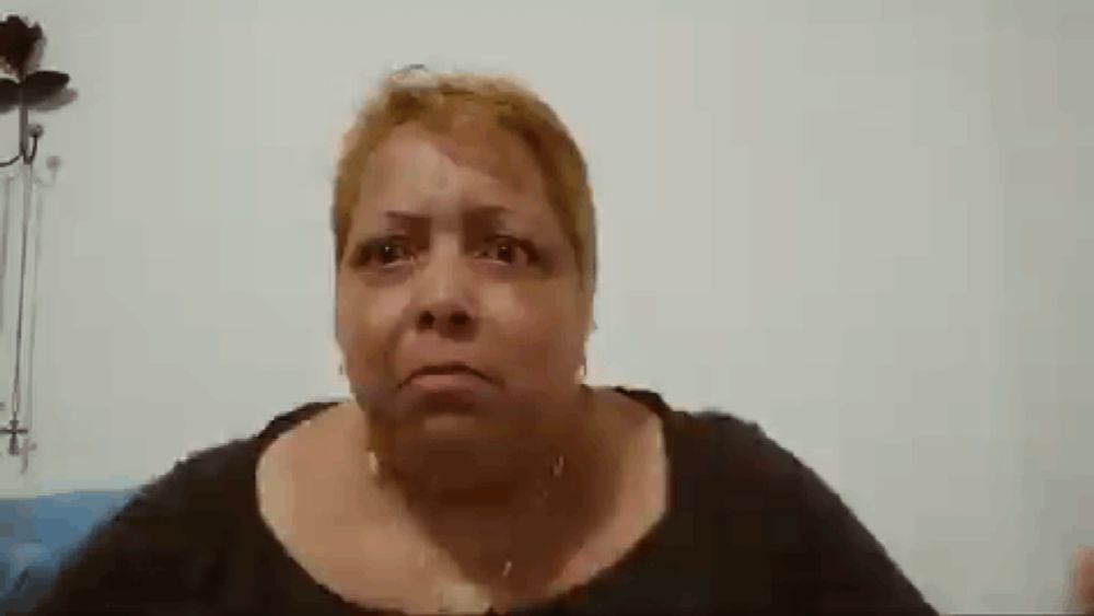 an older woman is making a funny face while sitting in front of a white wall .