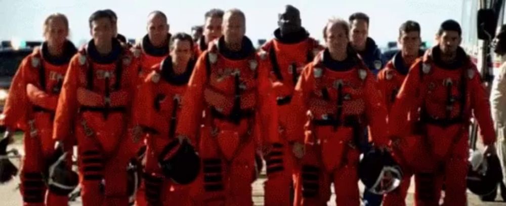 a group of men in red space suits are standing next to each other on a runway .