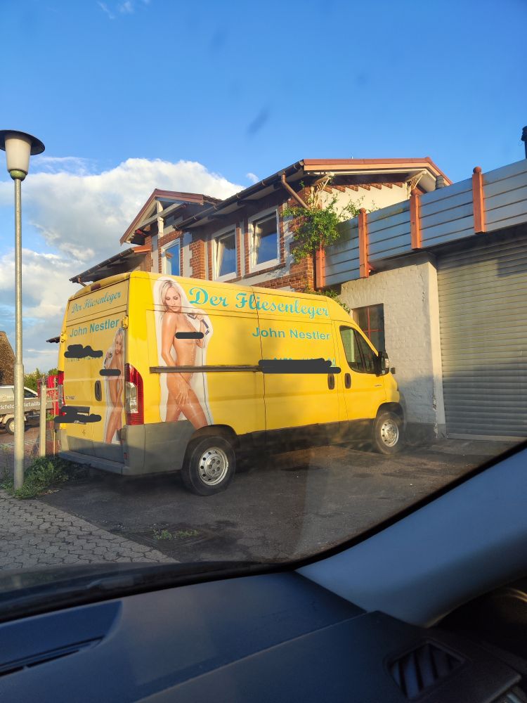 Gelber Van mit Werbung für einen Fliesenleger. Nackte pornographisch inszenierte Frau mit Duschkopf in der Hand

(Zensur ist von mir) 
