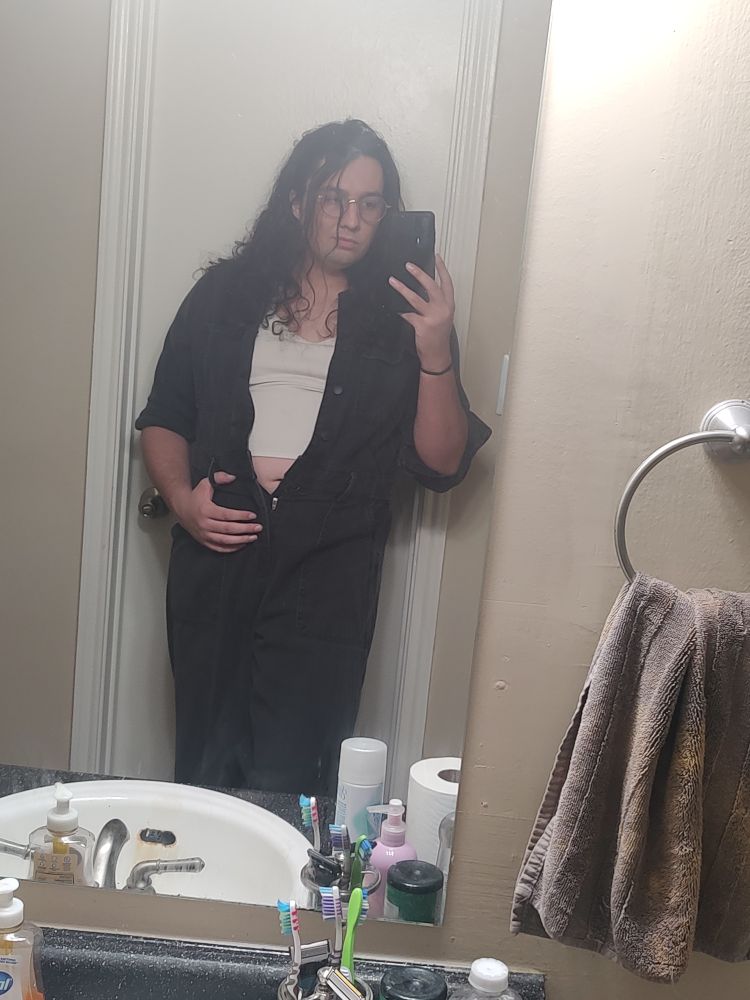 me in a black denim jumpsuit and a cropped white tank top, the jumpsuit unbuttoned down to just below the tank top
