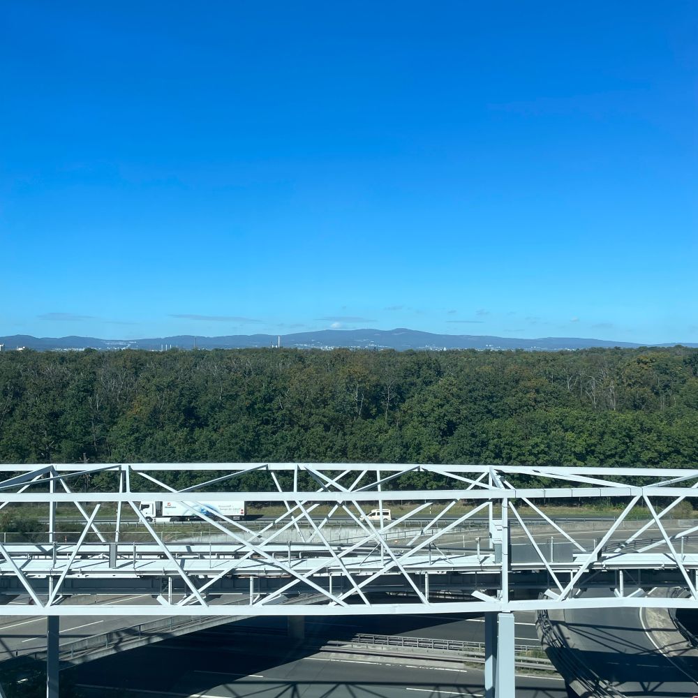 Blick auf den Taunus. Im Vordergrund sieht man eine Bundesstraße und Metro gefolgt vom Frankfurter Stadtwald. 