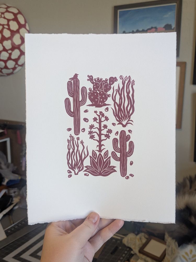 A photo of a hand holding up a large print of a pink desert plant design on white paper