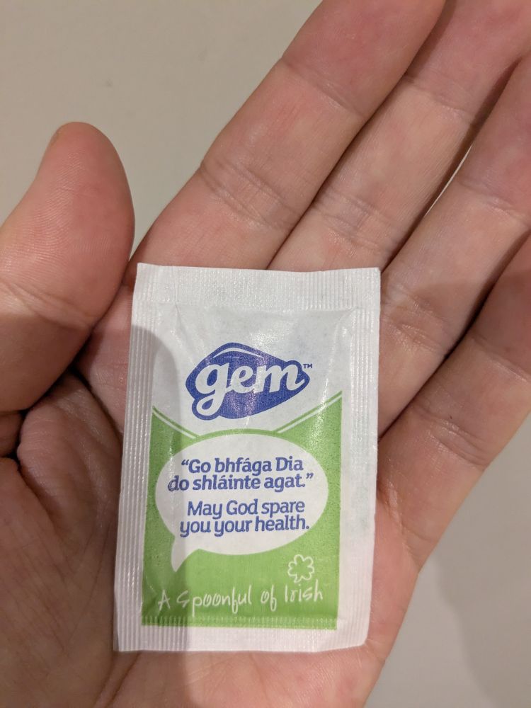 Screenshot of a sugar packet held in the palm of the hand, with the English sentence "May God spare you your health" beneath an Irish Gaelic sentence presumably saying the same thing.