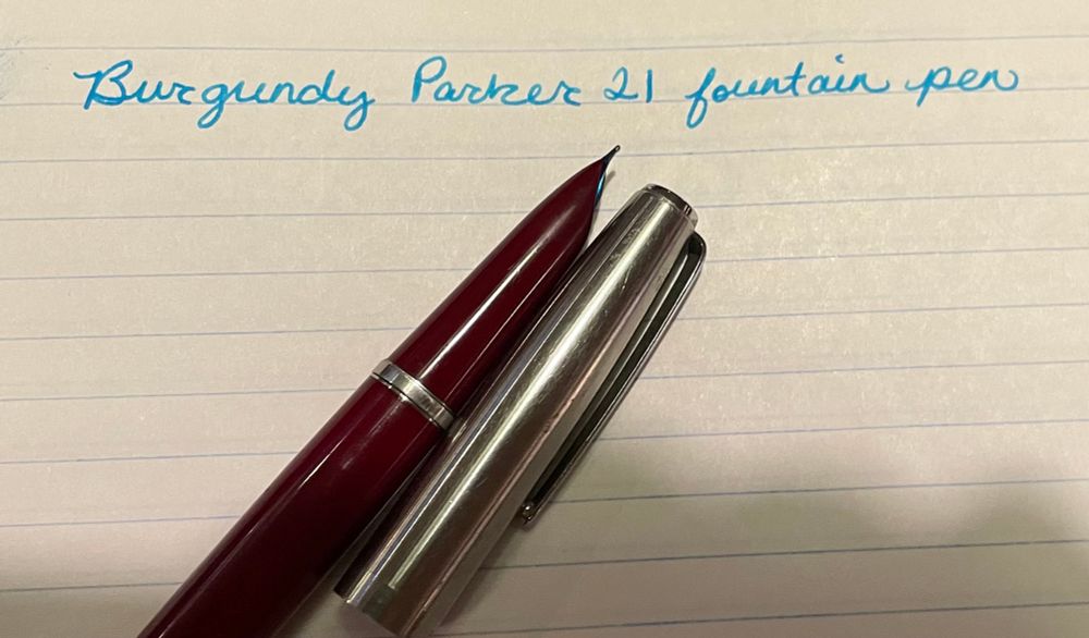 Burgundy Parker 21 fountain pen (written) and the burgundy fountain pen with a hooded nib and a silver cap next to it. 