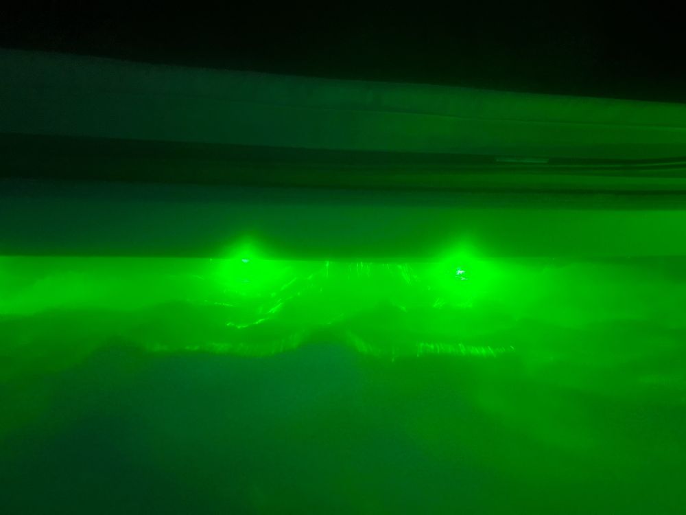 A dark outdoor setting of a hot tub with green lights casting light rays through the bubbles and water