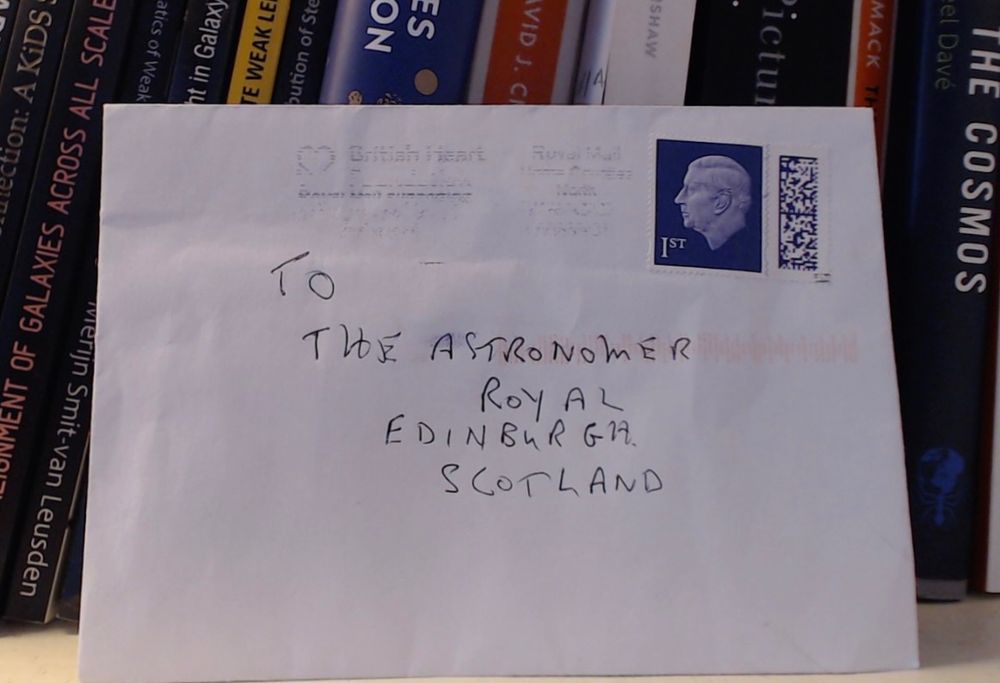 A handwritten envelope with a stamp of King Charles.  The address reads "To the Astronomer Royal, Edinburgh, Scotland".  In front of some books.