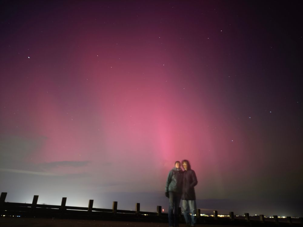 Two people (me and my 18yo) standing with bright red lights in the sky behind us. Northern Lights