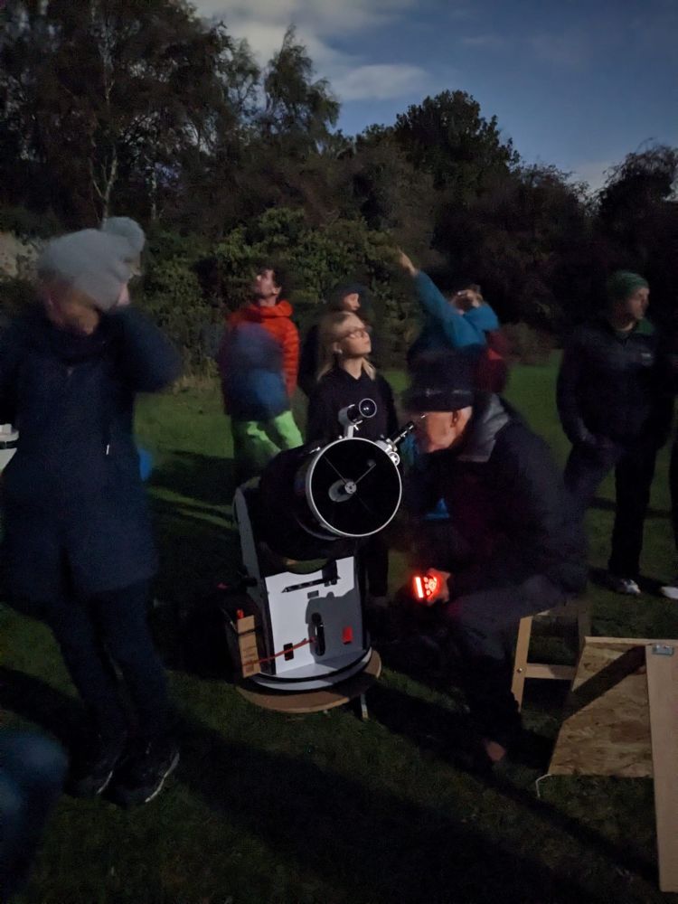 People pointing up at the stars.  In the centre a reasonably large telescope looks up towards the moon.