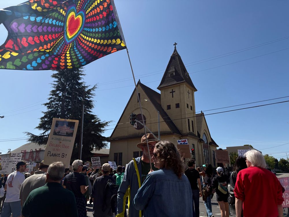 Protestor carrying a colorful starburst rainbow flag of hearts during #HandsOff March in Oakland, California.