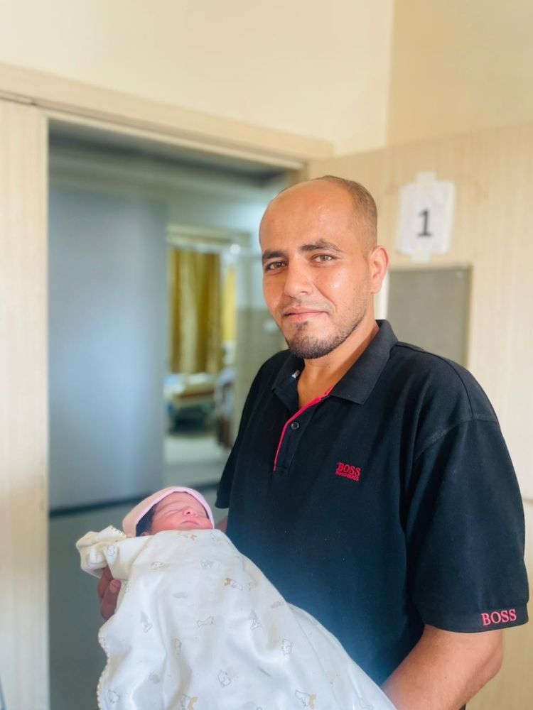 A new father has composed himself as best he can for his photo with his newborn. His eyes are full of love and determination.