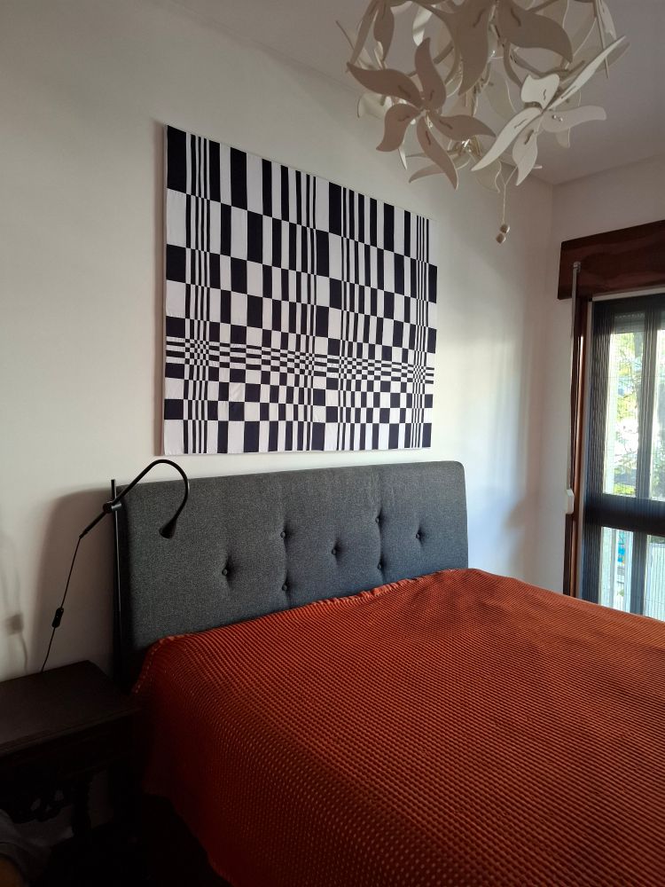 Black and white optical illusion artwork over a bed.