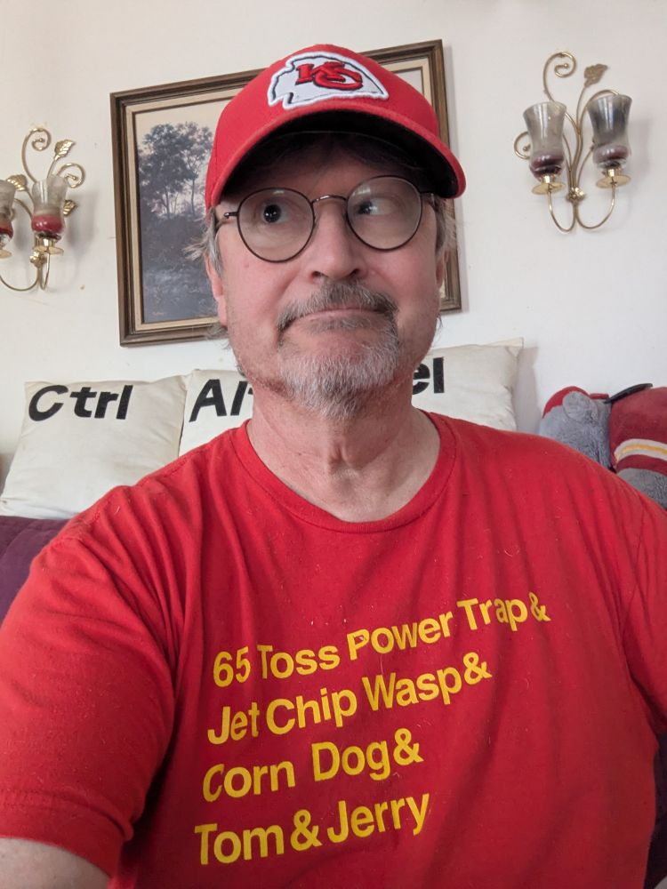 A guy with a red T-shirt that has the names of all the winning TD plays of the Chiefs' 4 Super Bowl wins. 
