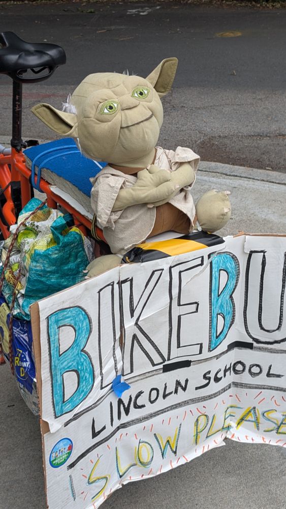 a stuffed yoda toy sitting on a sign that reads "Bike Bus" 