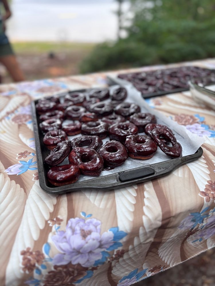Homemade fried doughnuts, covered in chocolate, on a tray on a table outside. 