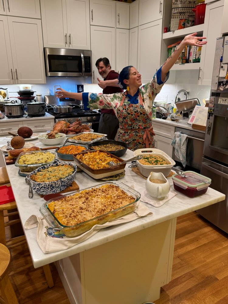 a Thanksgiving spread on a big kitchen island and a white woman throwing her arms up in the background