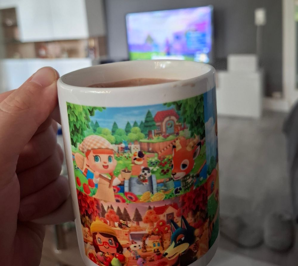 Animal Crossing-Tasse, die vor einen Fernseher gehalten wird.