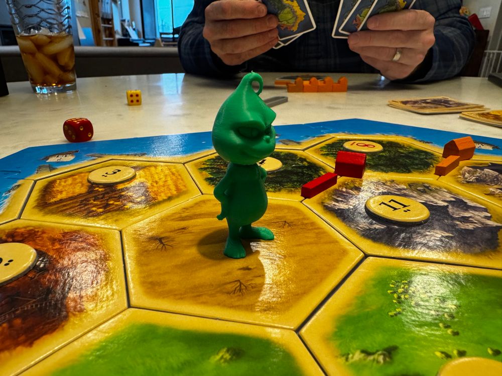 Photo showing the Catan board with a 3D-printed Grinch for a robber.