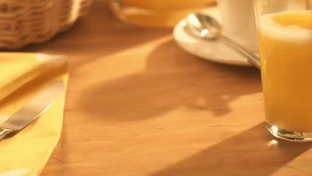 a glass of orange juice sits on a wooden table next to a knife and napkin