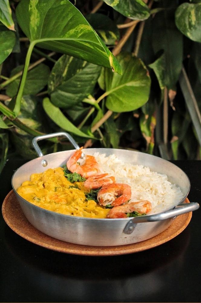 Prato típico da culinária de Manaus com camarão farofa amarela e arroz , numa forma sobre uma mesa e no fundo um jardim 
