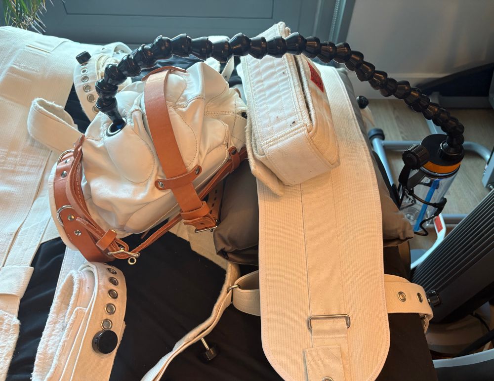 A Segufix head restraint, a white leather blackout hood with a grommet at the mouth, and an empty feeder bottle with a straw going into the grommet, Sir.