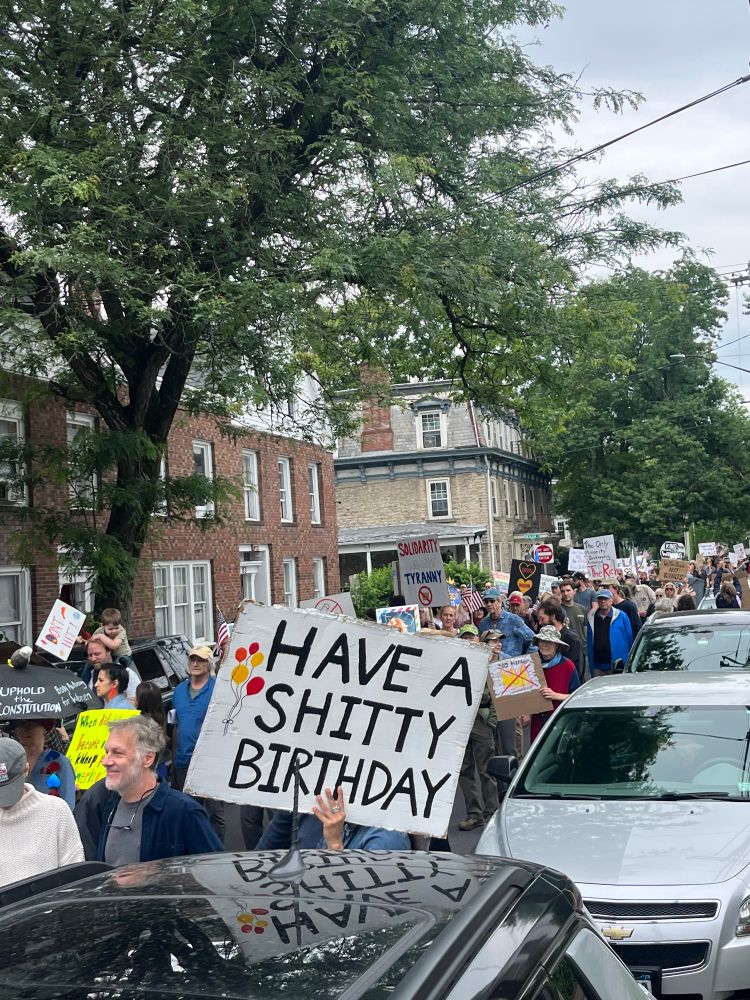 a bunch of people marching and a prominently featured sign reading "have a shitty birthday"