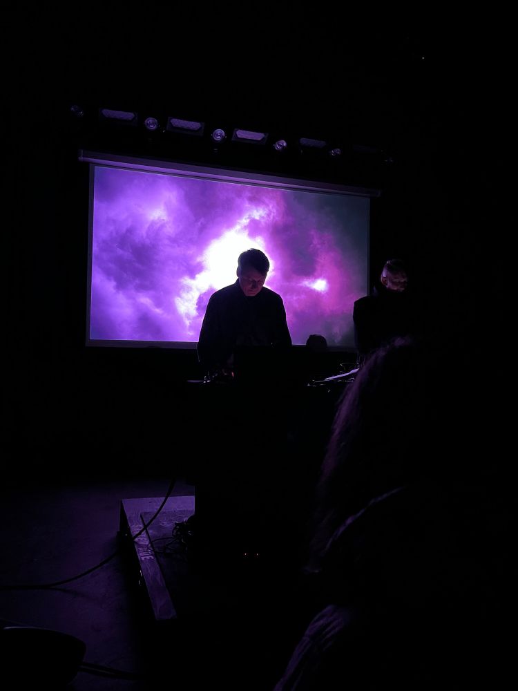 Ambient musicians Loscil and Lawrence English performing in front of a cloudy purple screen