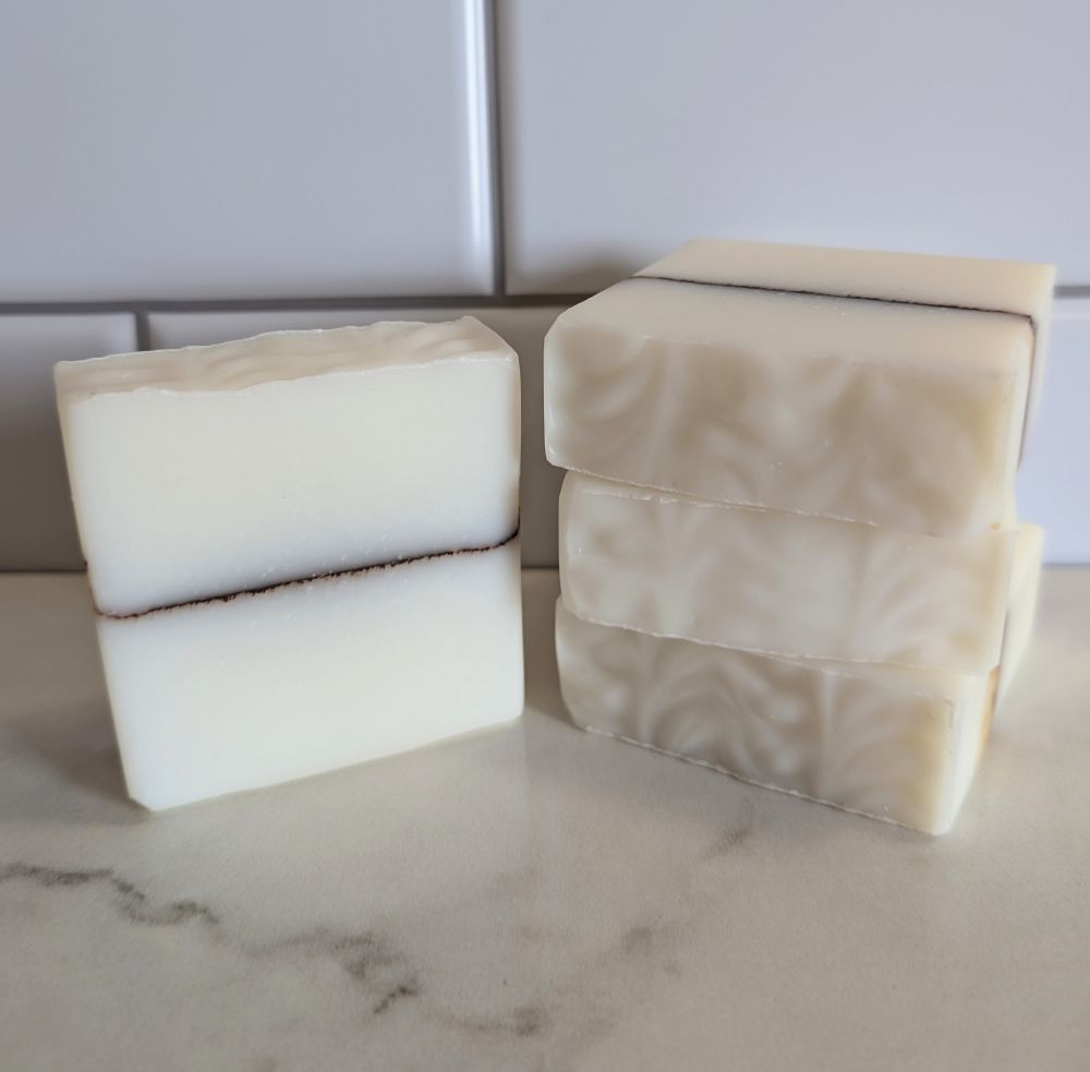 Four bars of artisan soap stacked on a faux marble surface with a tile background.