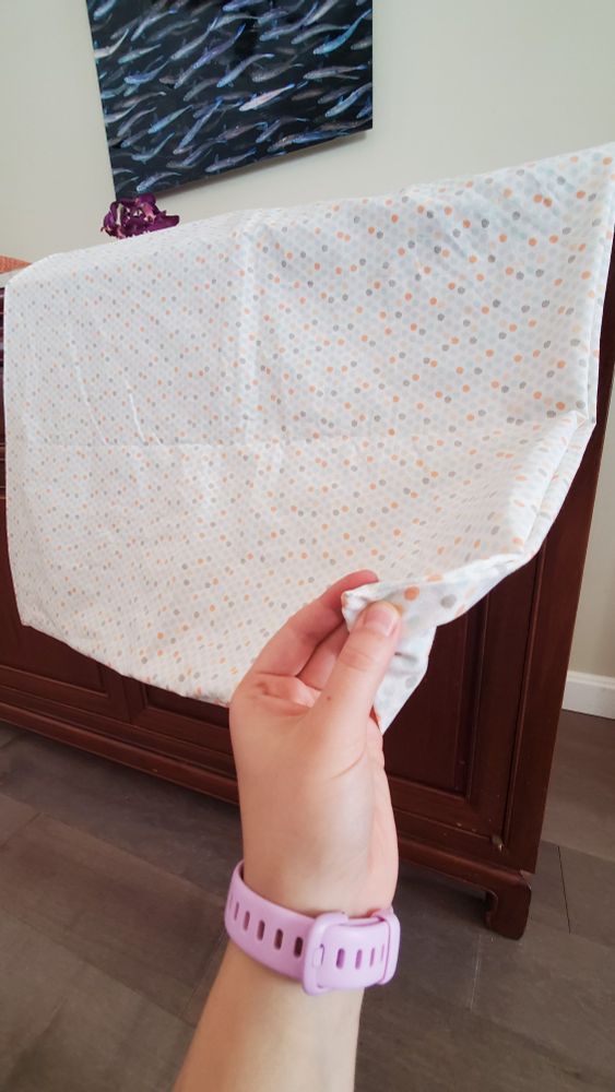 A photo of a white piece of fabric with orange, blue, and gray dots. A hand is holding the corner revealing its stitching.
