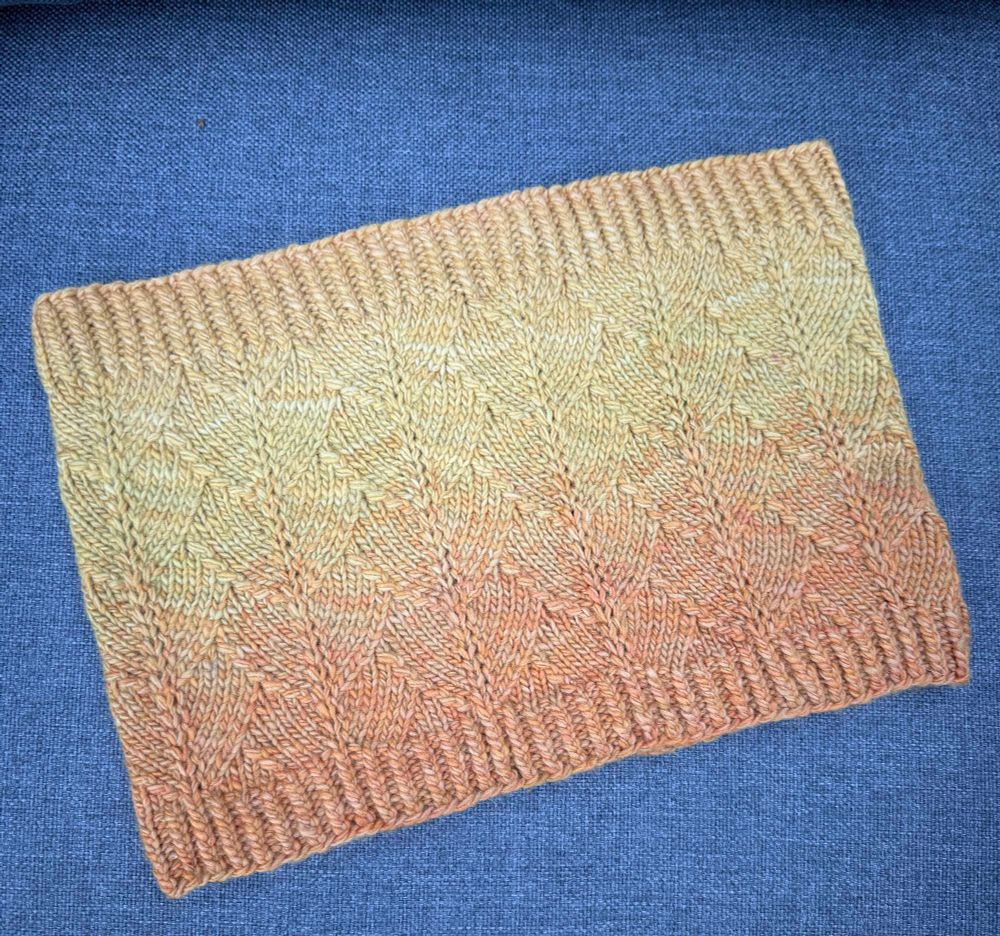 Hand knitted cowl in a dragon scale pattern featuring an ombré yarn in yellow and gold gradient colors. Twisted rib top and bottom borders. 
