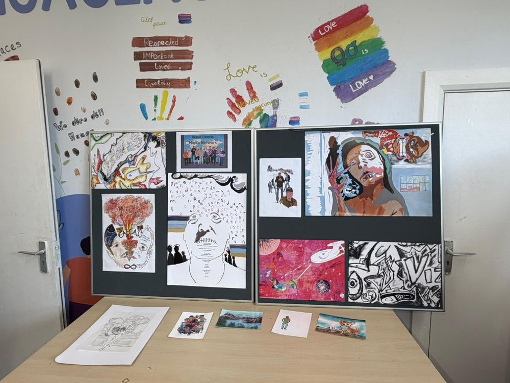 Art display showcasing diverse artwork, including colourful abstract pieces, portraits, and a rainbow flag on the wall.