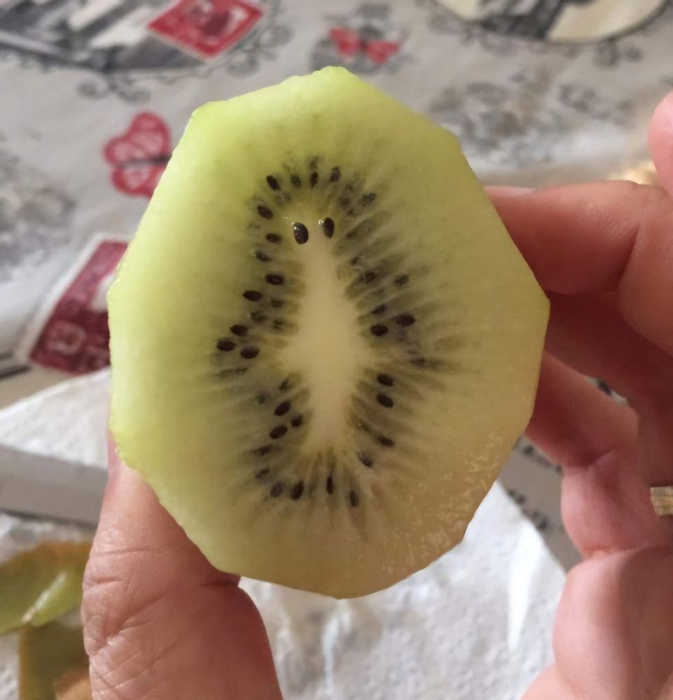 A kiwi fruit cut in half. Inside the white center looks like a ghost. Two small black kiwi seeds have been put on the ghost's head to look like eyes