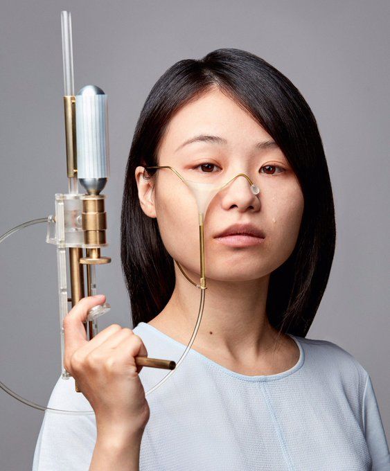 Photo of the designer, a young Taiwanese woman, holding up her gun. There are delicate tubes and a small clear pocket attached to her face, ready to catch any tears  