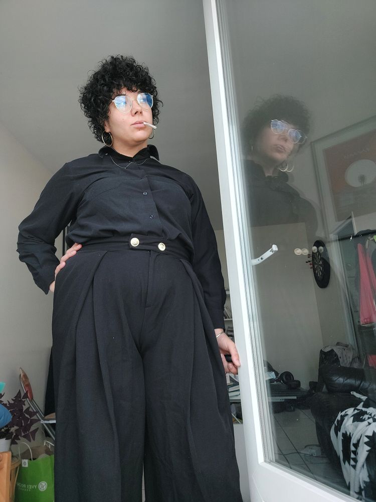 Selfie en pied avec une chemise noire, pendentif doré, pantalon noir à boutons dorés sur la ceinture 