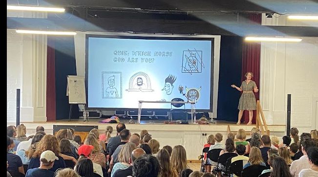 Me gesticulating on stage while I run a quiz for the audience in kitson hall about "which norse god are you?". We see the backs of heads. Taking photos of events with kids is a real art, avoiding any faces. 