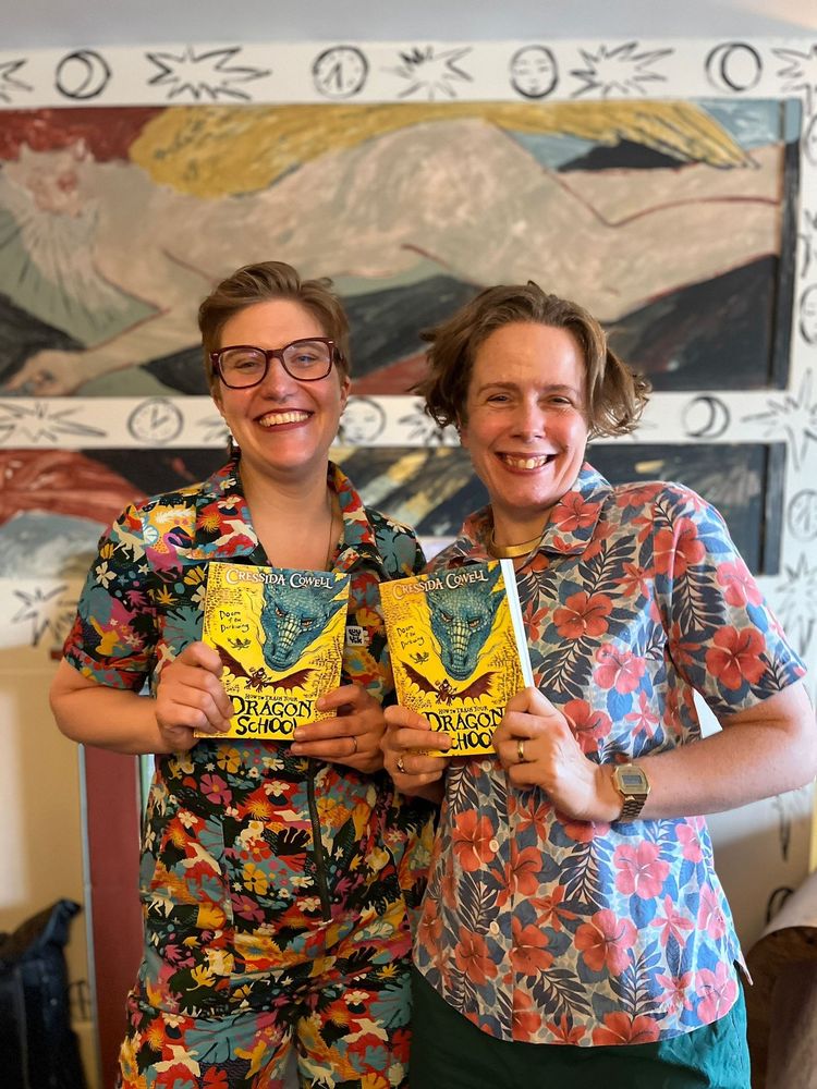 Me and robin stevens wearing wildly clashing patterned outfits and clutching copies of Dragon School by Cressida Cowell. Behind us is some art cos we're in a fancy place for fancy people.
