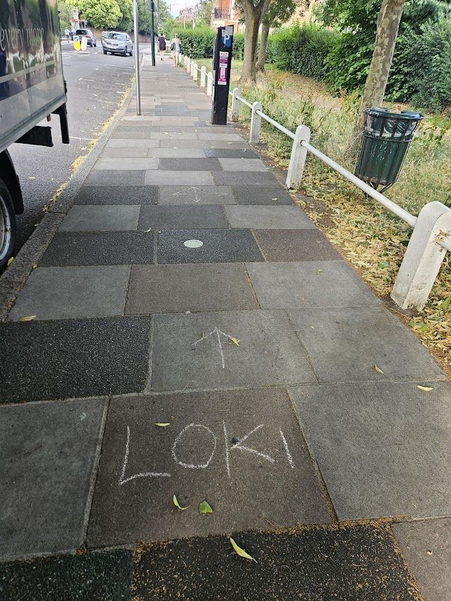 A pavement with a word chalked on it. That word is Loki. There's an arrow pointing onwards. Then, a few paving stones ahead, there are four arrows pointing in four different directions. I blame Loki. It's incredible everyone found their way to the venue tbh.